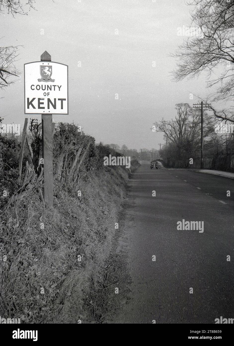 1950, historique, sur une route rurale, un panneau routier pour le comté de Kent, Angleterre, Royaume-Uni, un comté dans le sud-est de l'Angleterre, connu comme «le jardin de l'Angleterre» en raison de ses riches terres agricoles, de nombreux vergers et jardins de houblon. Une voiture de l'époque sur la route à venir. Banque D'Images