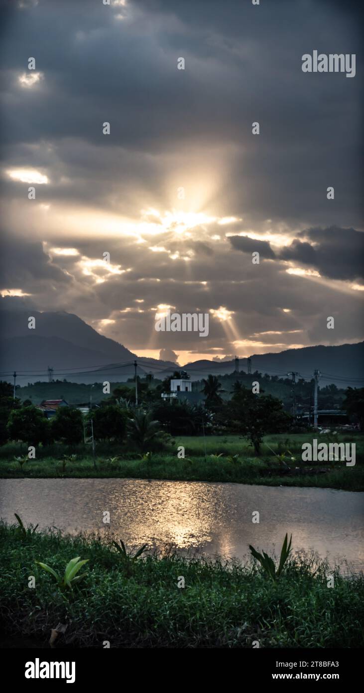 Rayons du soleil à travers les nuages, coucher de soleil au-dessus des montagnes, reflet doré dans l'eau de surface du lac, énergie de bonté de confort Banque D'Images