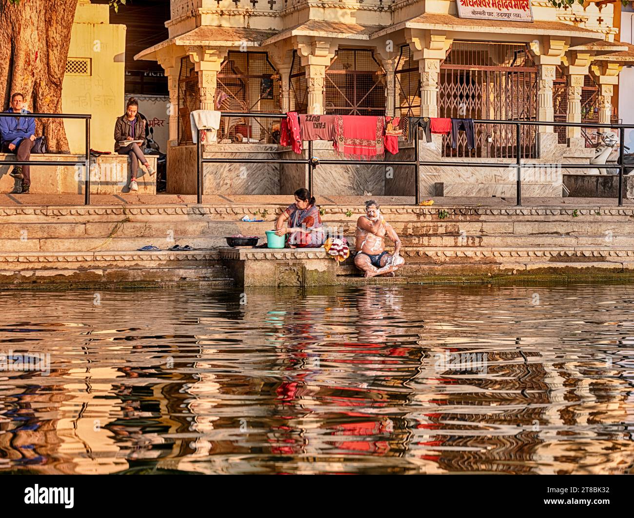 UDAIPUR, INDE - 27 DÉCEMBRE 2022 : un homme et une femme non identifiés se baignent sur les marches d'un ghat au bord du lac Pichola à Udaipur, en Inde. Banque D'Images