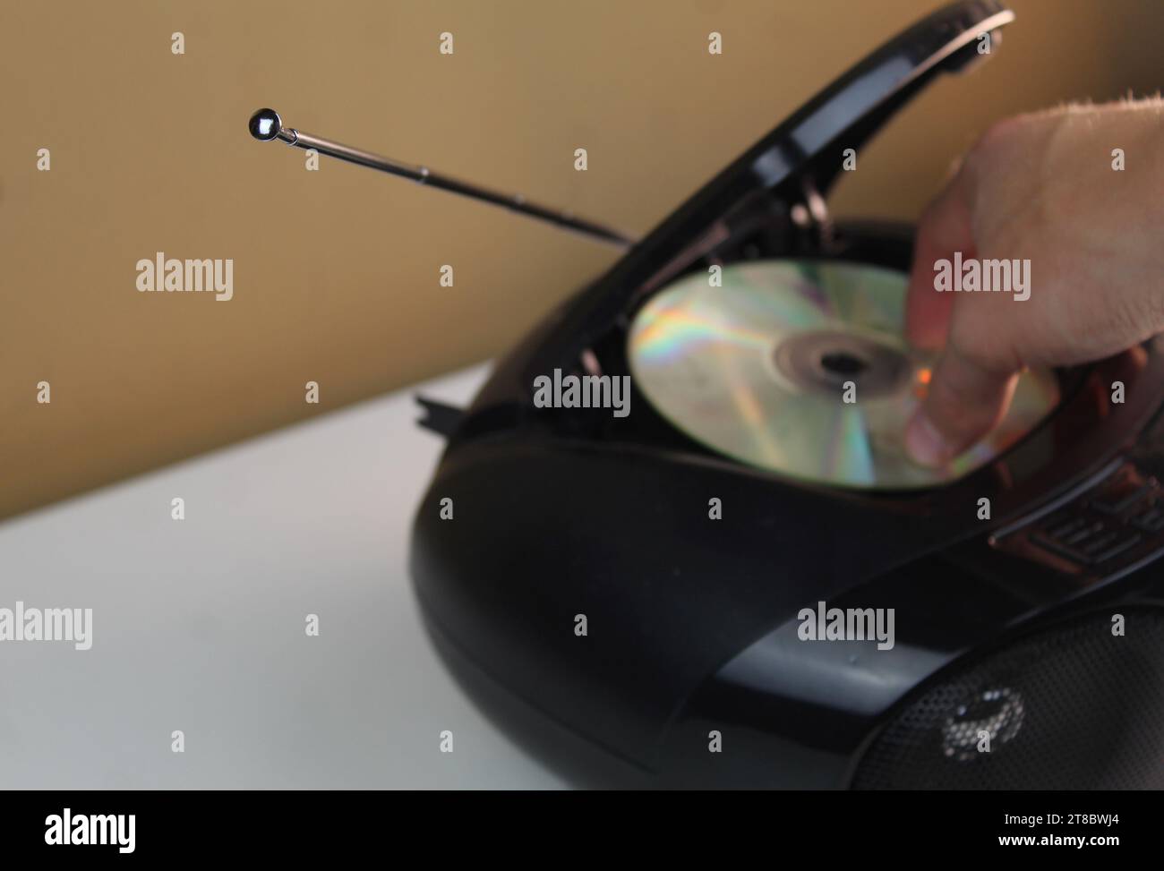 Photo d'une main blanche caucasienne poussant un cd dans un lecteur de cd noir sur un bureau blanc. Lecture de musique. Banque D'Images