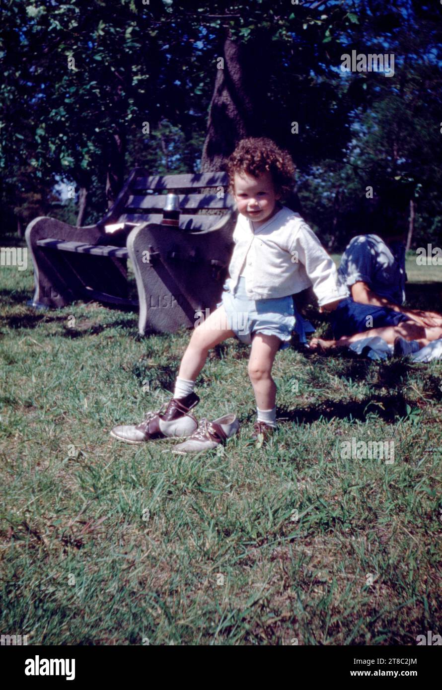 Jeune fille près de Park Bench glissant sur sa chaussure de mère alors que mère repose dans les années 1950 Banque D'Images