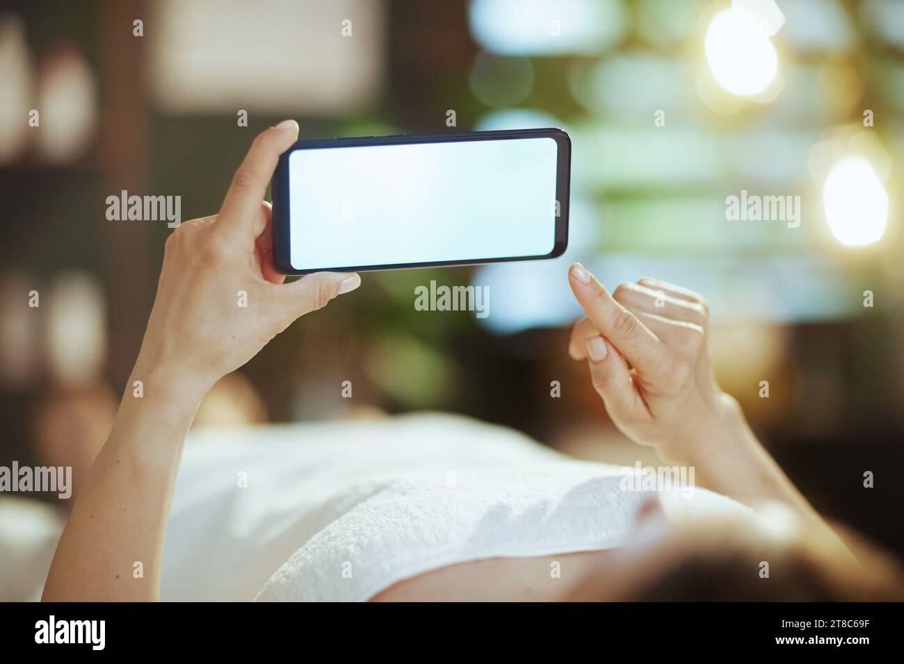 Le temps des soins de santé. Gros plan sur la femme détendue dans le salon de spa avec le téléphone portable écran vide posé sur la table de massage. Banque D'Images