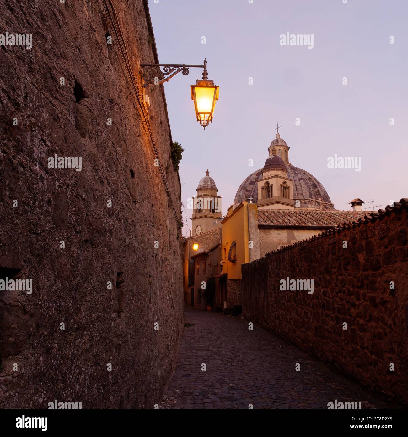 Basilique de Santa Margherita au crépuscule vu d'une rue étroite avec lampadaire incandescent, Montefiascone, région du Latium, Italie. 19 novembre 2023 Banque D'Images
