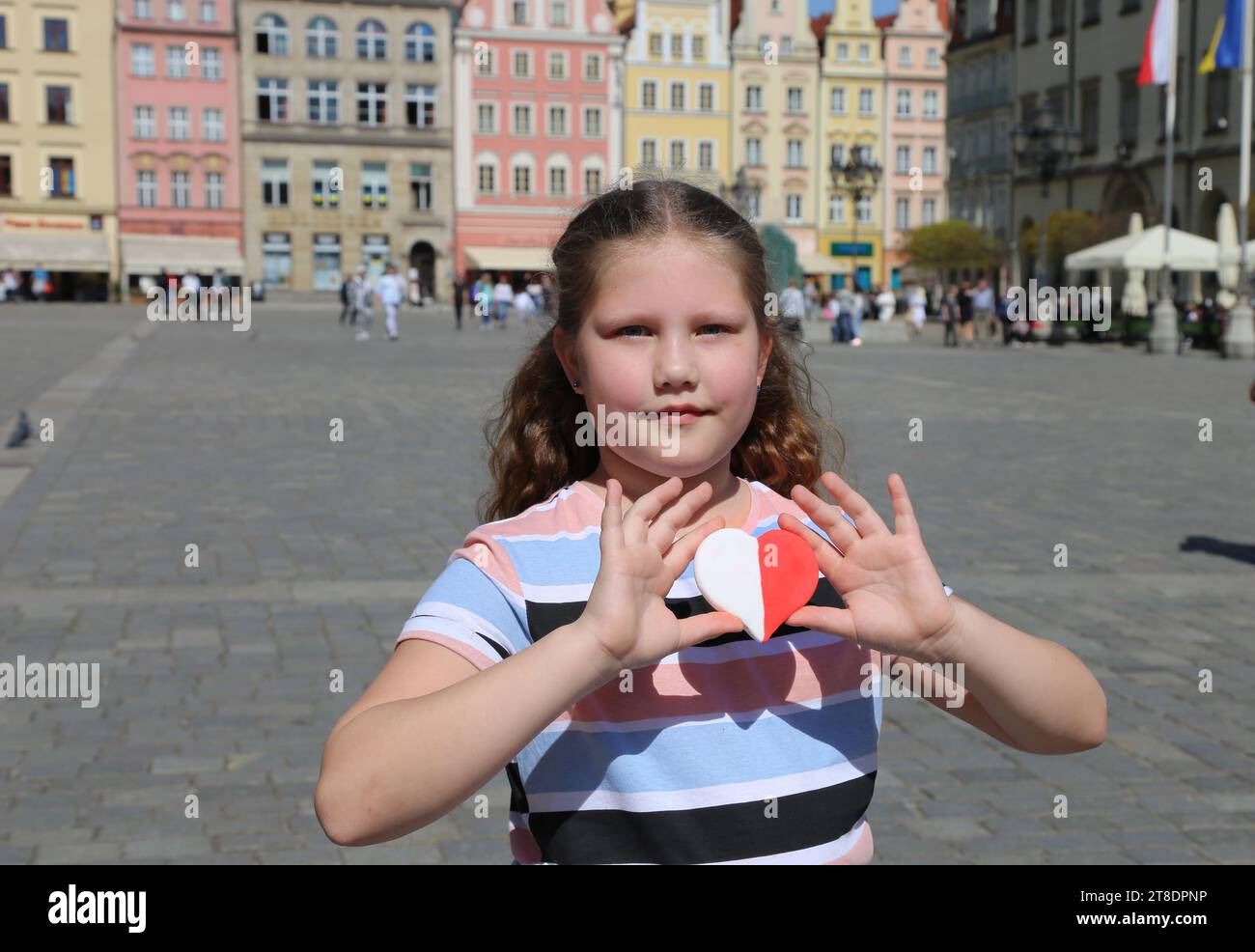 Un cœur rouge-blanc aux couleurs du drapeau national de la Pologne dans les mains d'un enfant sur fond de la place de la vieille ville. Jour de l'indépendance o Banque D'Images