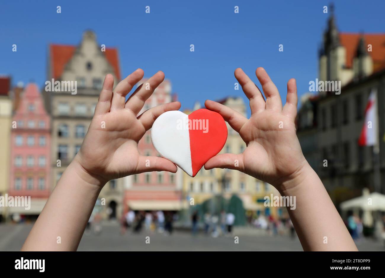 Un cœur rouge-blanc aux couleurs du drapeau national de la Pologne dans les mains d'un enfant sur fond de la place de la vieille ville. Jour de l'indépendance Banque D'Images