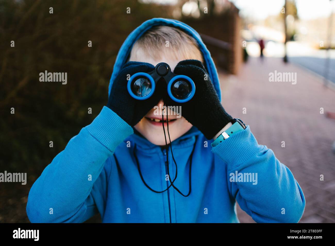 Garçon en milieu urbain en sweat-shirt bleu regarde à travers des jumelles Banque D'Images