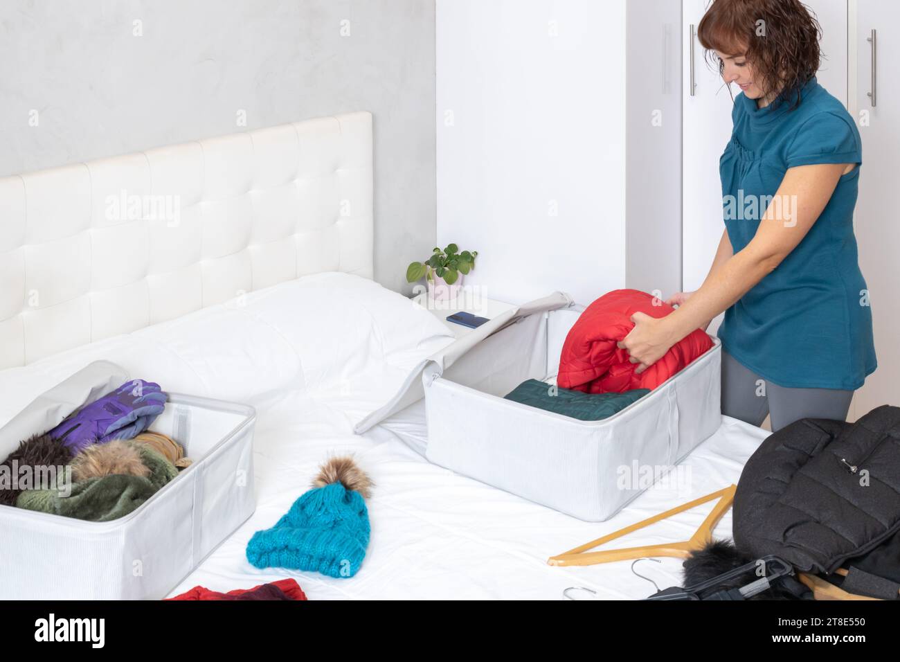 Photo horizontale, d'une femme dans une chambre avec des vêtements d'hiver couchés sur le lit, les recueillant à l'intérieur des boîtes en tissu. vestiaire. Banque D'Images