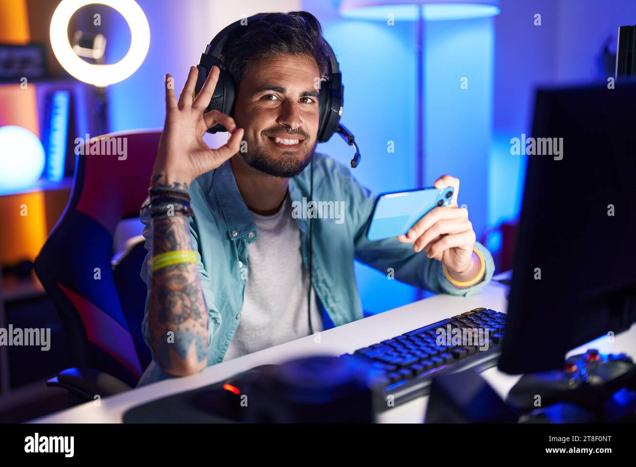 Jeune homme hispanique avec des tatouages jouant à des jeux vidéo avec smartphone faisant ok signe avec les doigts, souriant amical gestuant excellent symbole Banque D'Images