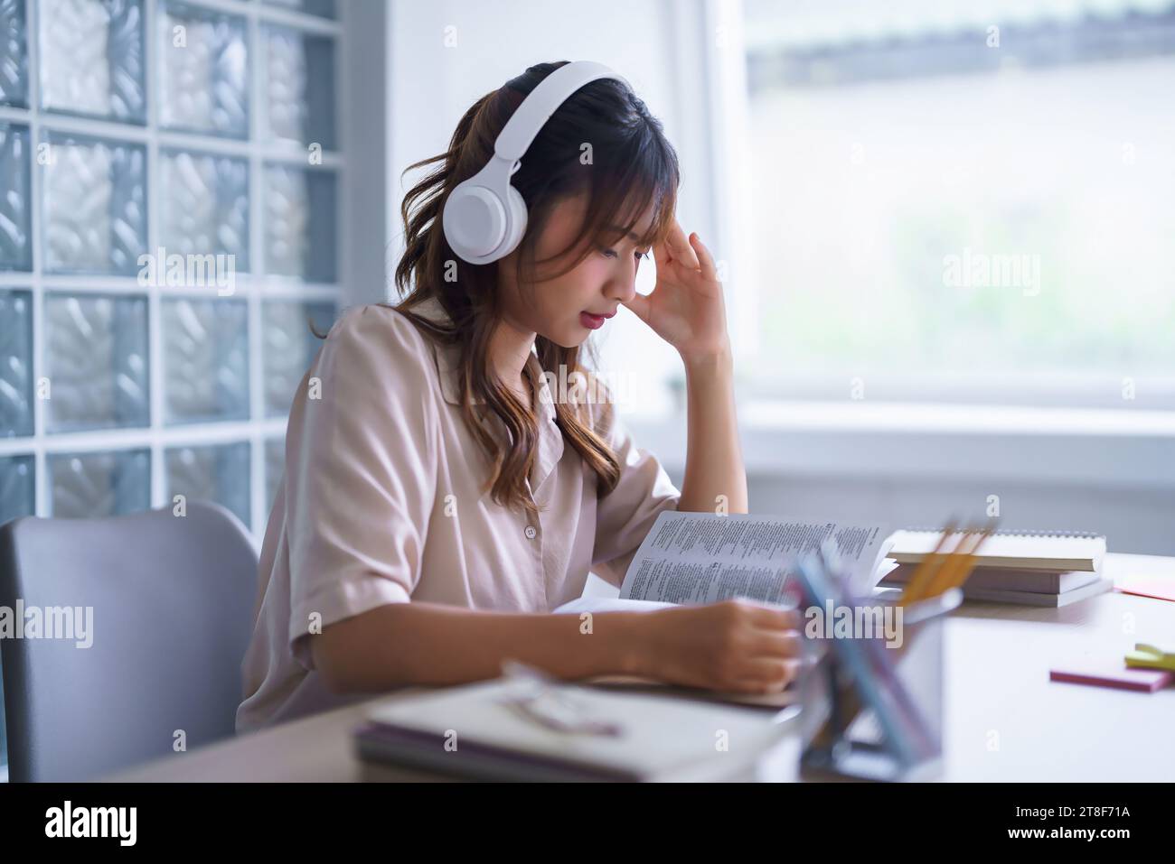 Jeune étudiant asiatique dans des vêtements décontractés portant des écouteurs à écouter la musique et la lecture de manuel à penser des idées tout en étudiant l'éducation Knowle Banque D'Images