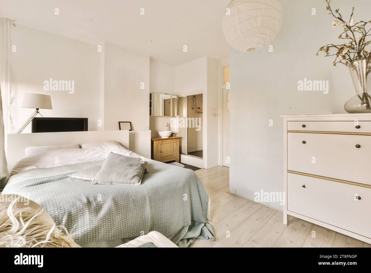 Lit confortable avec vase de fleur sur commode dans une chambre spacieuse avec des murs blancs à l'appartement contemporain Banque D'Images