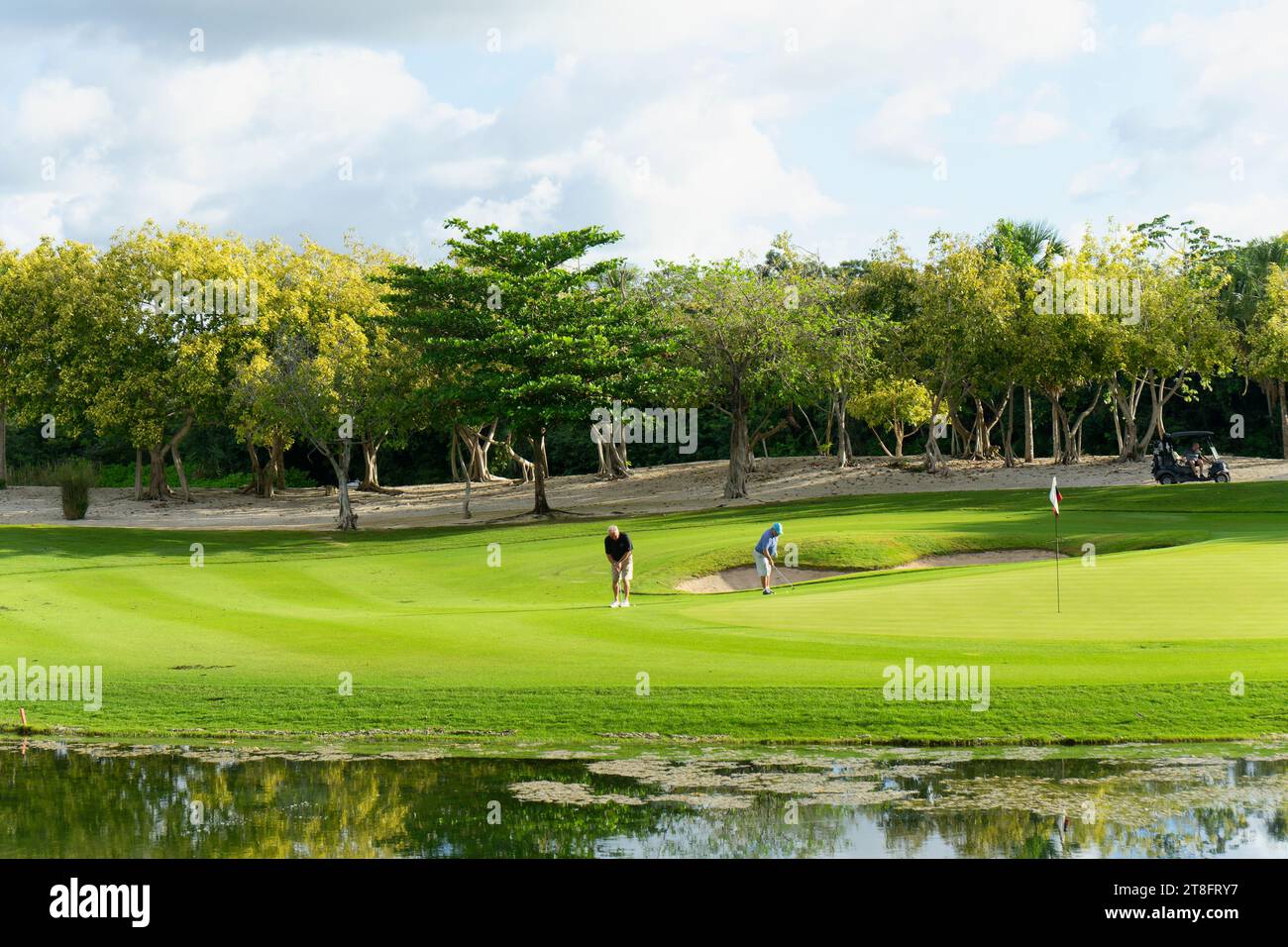 Golfeurs sur le green pour le tir final près d'un lac par une journée ensoleillée dans les tropiques au Mexique Banque D'Images