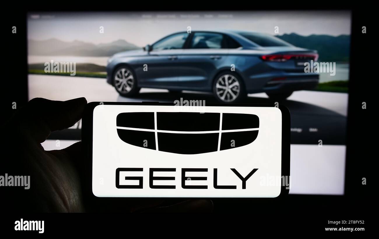 Personne tenant le téléphone portable avec le logo du fabricant de voitures chinois Zhejiang Geely Holding Group en face de la page Web de l'entreprise. Concentrez-vous sur l'affichage du téléphone. Banque D'Images