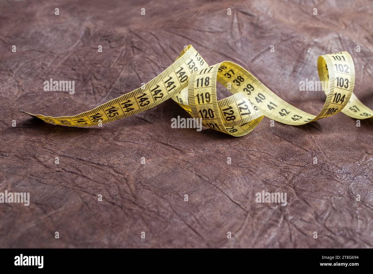 Ruban à mesurer jaune tourbillonné sur fond brun texture cuir véritable Banque D'Images