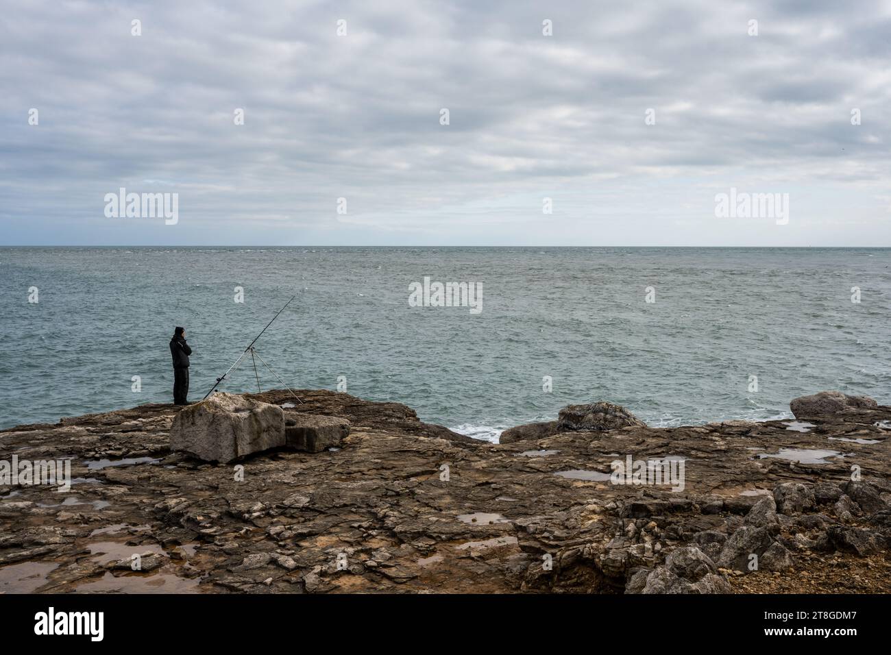 Un pêcheur se tient sur un rebord rocheux sur la rive de Portland Bill sur la côte jurassique du Dorset. Banque D'Images