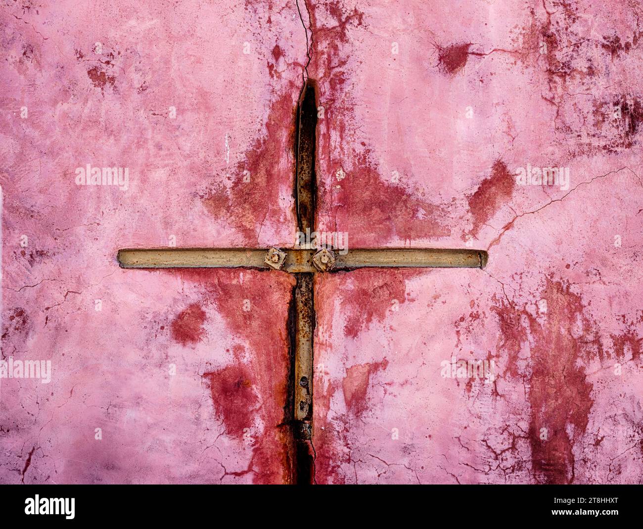 Une entretoise de fer sur un mur rose destinée à stabiliser une fissure dans la ville d'Oia prend la forme d'une croix. Banque D'Images