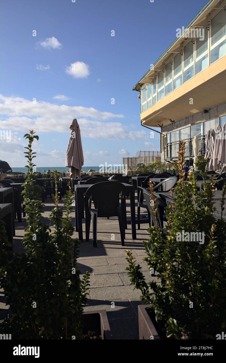 Tables et chaises d'un restaurant sur une promenade à côté du brise-lames en bord de mer Banque D'Images