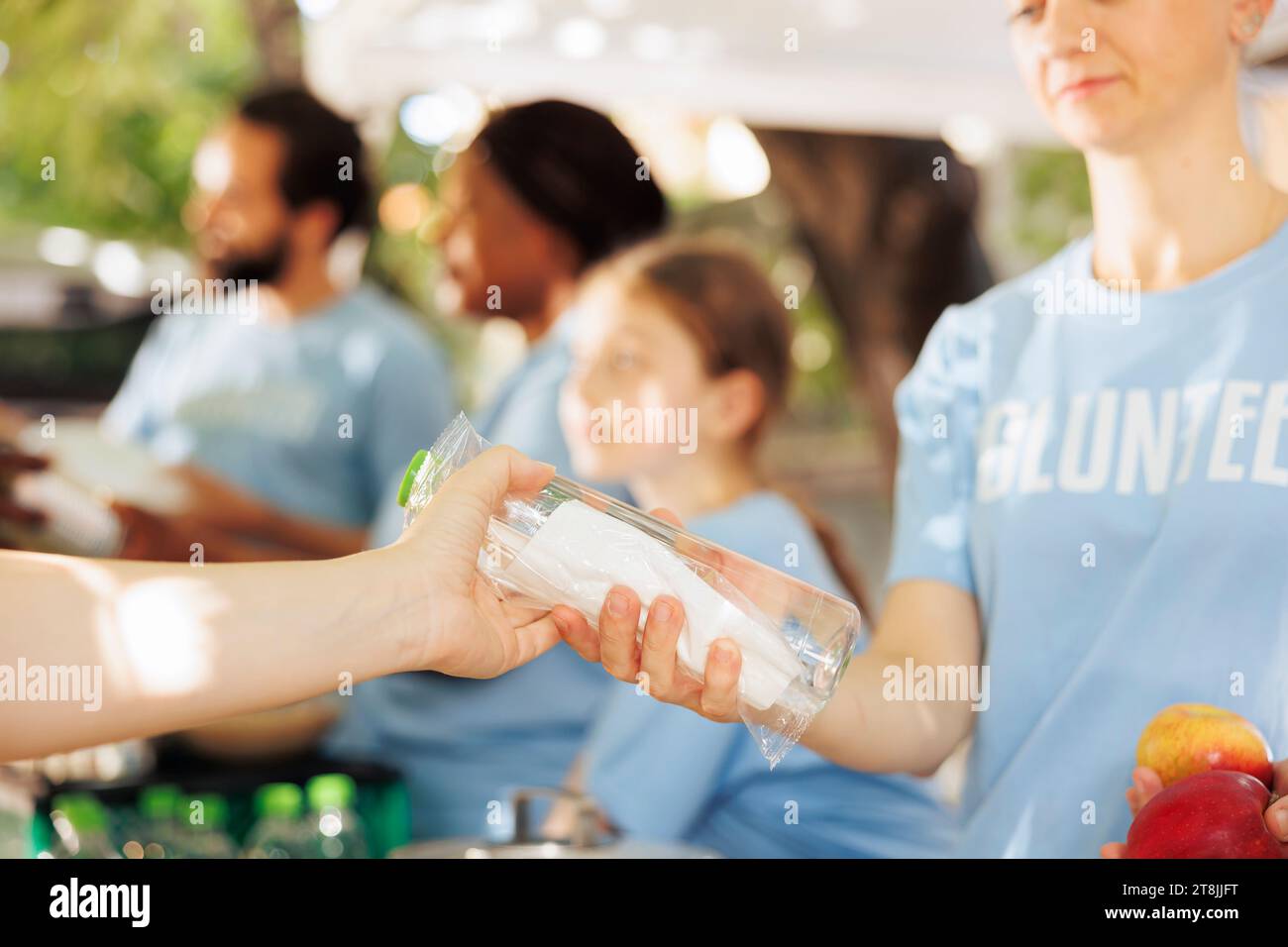 De jeunes volontaires distribuent avec compassion des boîtes de nourriture, apportant une aide aux pauvres. Image détaillée d'une travailleuse caritative qui donne de l'eau et des fruits frais à des personnes nécessiteuses et moins fortunées. Banque D'Images