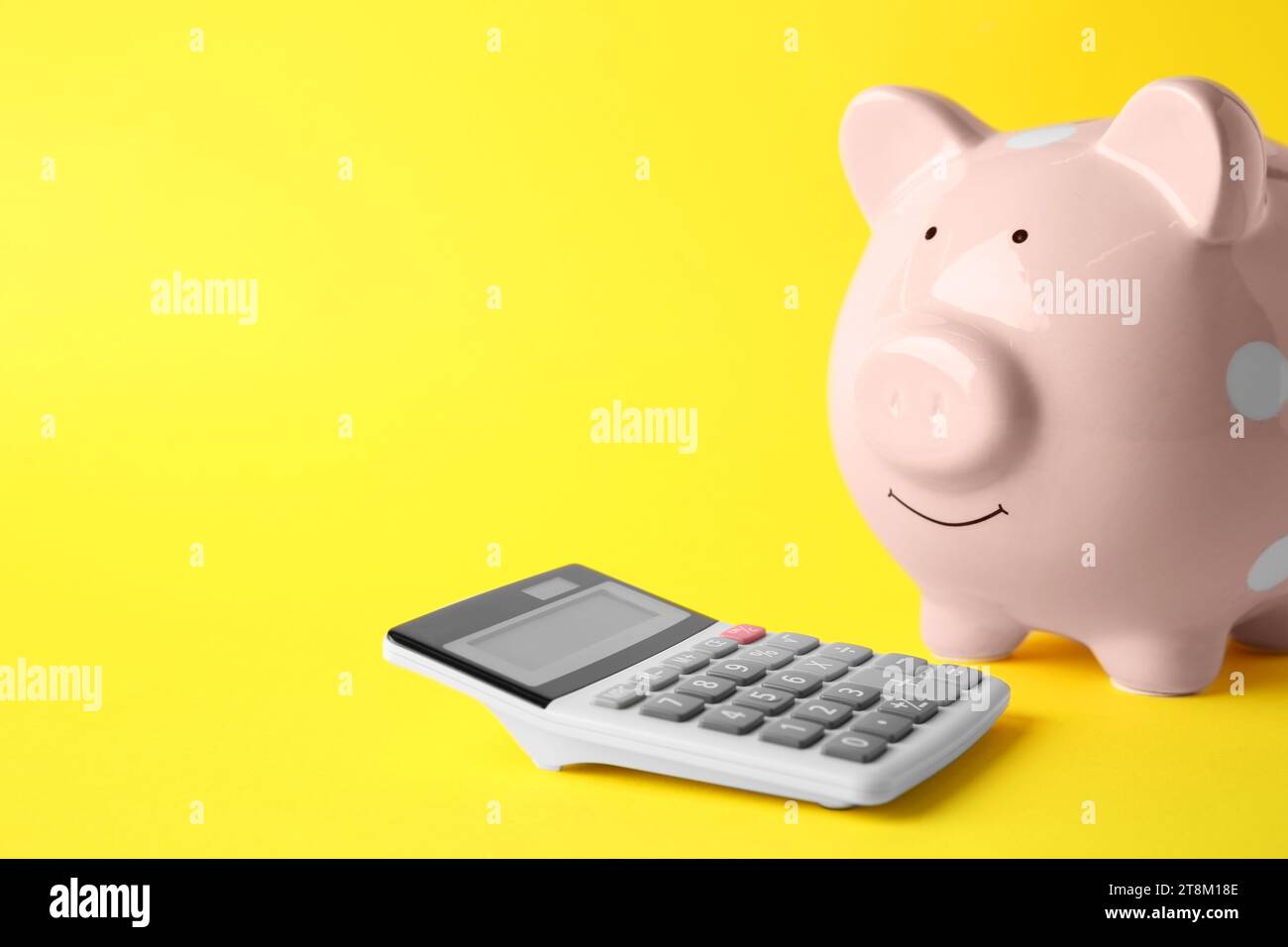 Calculatrice et tirelire rose sur fond jaune, gros plan. Espace pour le texte Banque D'Images