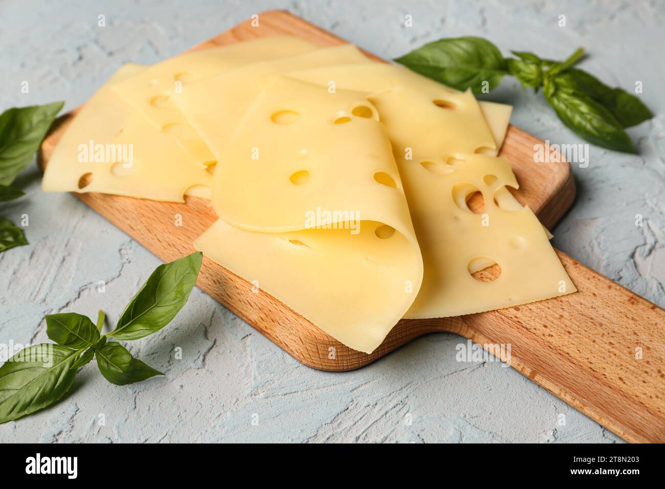 Planche avec des tranches de fromage savoureuses et des feuilles de basilic sur fond clair, gros plan Banque D'Images