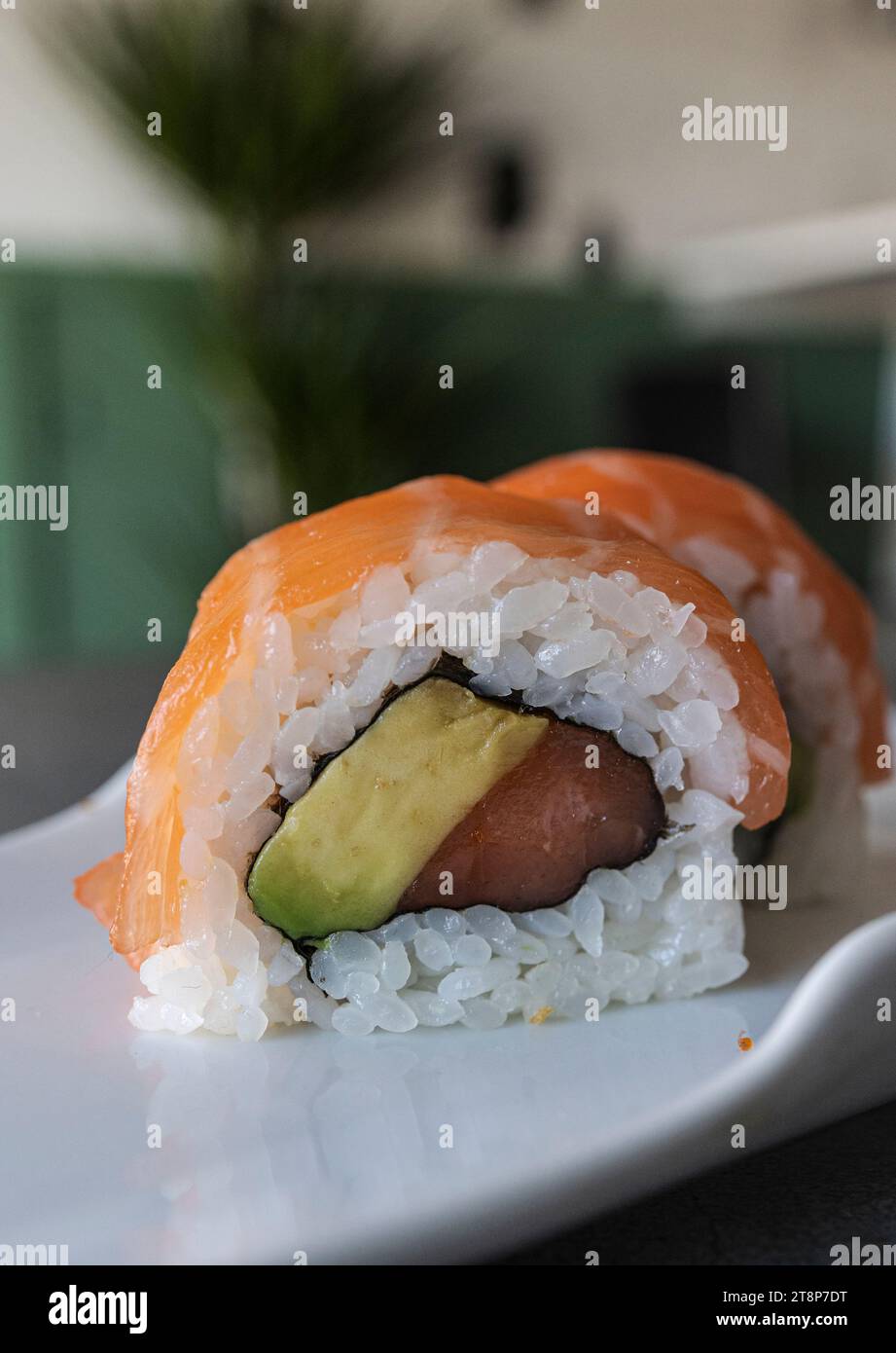 Une image rapprochée de rouleaux de sushi fraîchement préparés, avec des tranches fraîches de thon et d'avocat, servis sur une assiette blanche Banque D'Images