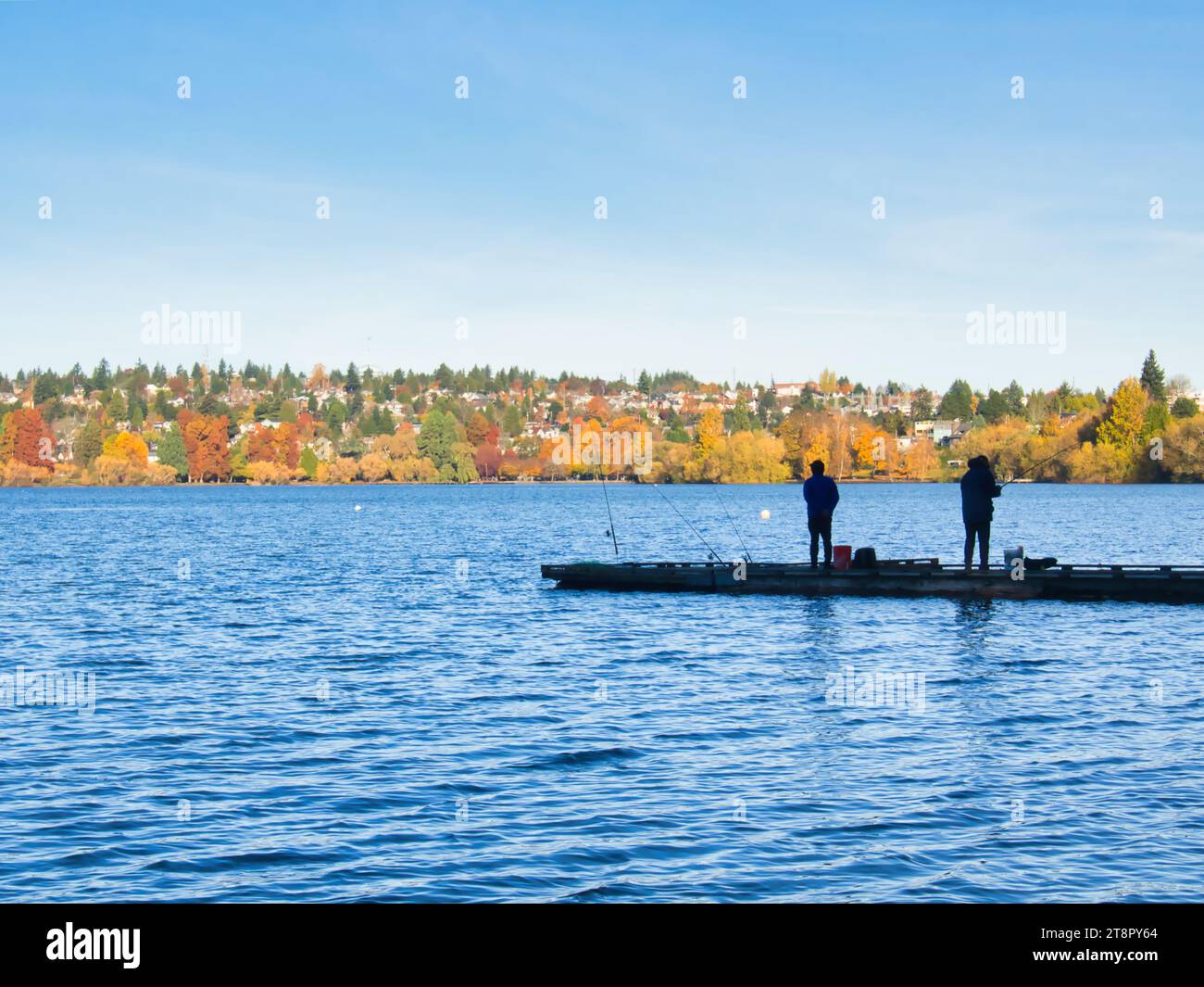 Deux hommes en silhouette d'une distance faisant des loisirs de pêche sportive en plein air à partir d'une jetée en automne à Green Lake Park à Seattle, Washington. Banque D'Images