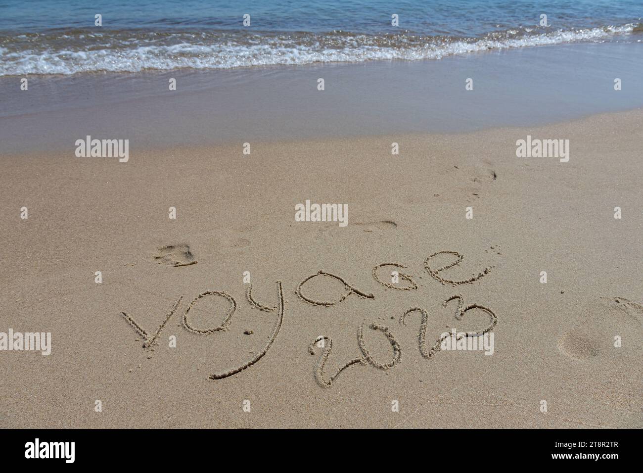 L'inscription voyaje 2022 en français, Voyage 2022, sur le sable par l'eau et la vague montante, mer vacances plage au bord de la mer. Banque D'Images