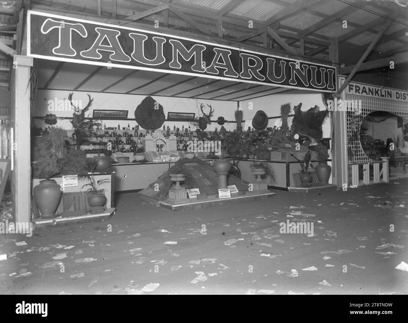 Un stand à une foire commerciale en 1930, la publicité de produits de Taumarunui, vue d'un stand à une foire commerciale, probablement tenue à Auckland, Nouvelle-Zélande. Le stand annonce des produits et des expositions de Taumarunui, y compris une sélection de tuiles et divers pots de jardin et ornements produits par Winstones Roofing Tile Works et Winstone Ltd, Taumarunui. Des pots et des bouteilles de produits sont également montrés, avec plusieurs trophées de tête de cerf sur le mur derrière Banque D'Images