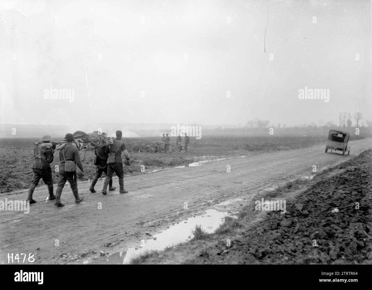 Amenant les blessés près de Courcelles, en France, les porteurs de brancard portent un soldat blessé sous des tirs d'obus sur la somme. Les montre marcher le long d'une route boueuse avec des explosions d'obus à une certaine distance sur la gauche. Une voiture est plus loin sur la route. Photographie prise par Courcelles le 6 avril 1918 Banque D'Images