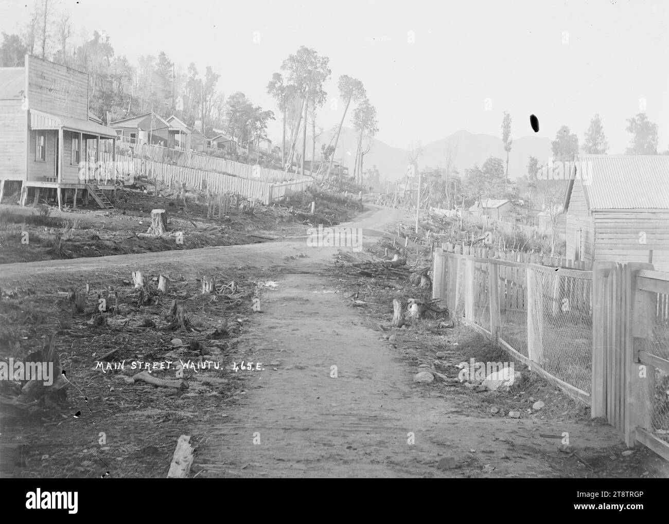 Main Street, Waiuta, Buller District, vue de la rue principale dans le village aurifère de Waiuta. Montre des maisons entourées de clôtures de piquetage des deux côtés de la rue. en 1910 Banque D'Images