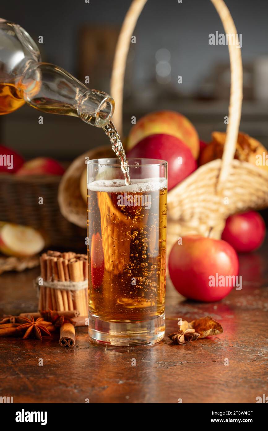 Le cidre de pomme est versé d'une bouteille dans un verre. Boisson fraîche avec pommes, cannelle et anis sur une table de cuisine. Banque D'Images