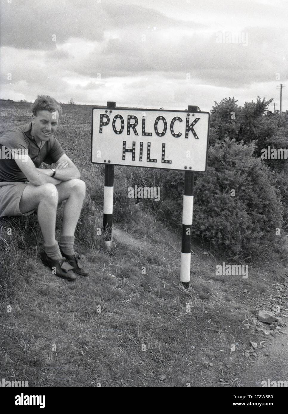Années 1950, historique, un cycliste de tourisme masculin assis pour sa photo ayant atteint le sommet de la célèbre Porlock Hill dans le Somerset, Angleterre, Royaume-Uni. Faisant partie de l'A39, la route est considérée comme la route A la plus raide de Grande-Bretagne, avec 1-4 par endroits. Banque D'Images