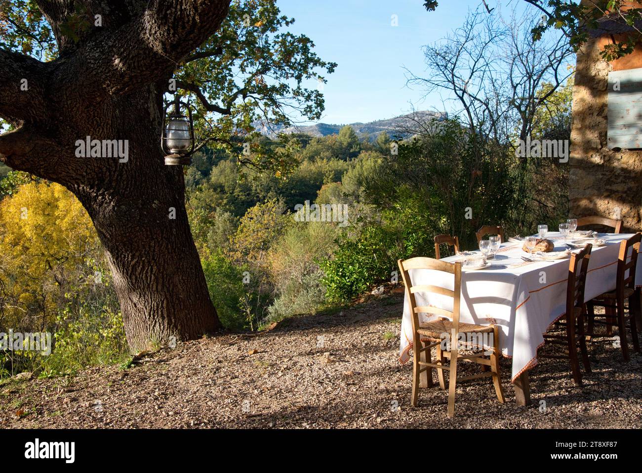 une table à manger habillée, avec assiettes, couverts verres et miche de pain, sur une terrasse à l'heure du souper, avec en arrière plan les collines Banque D'Images