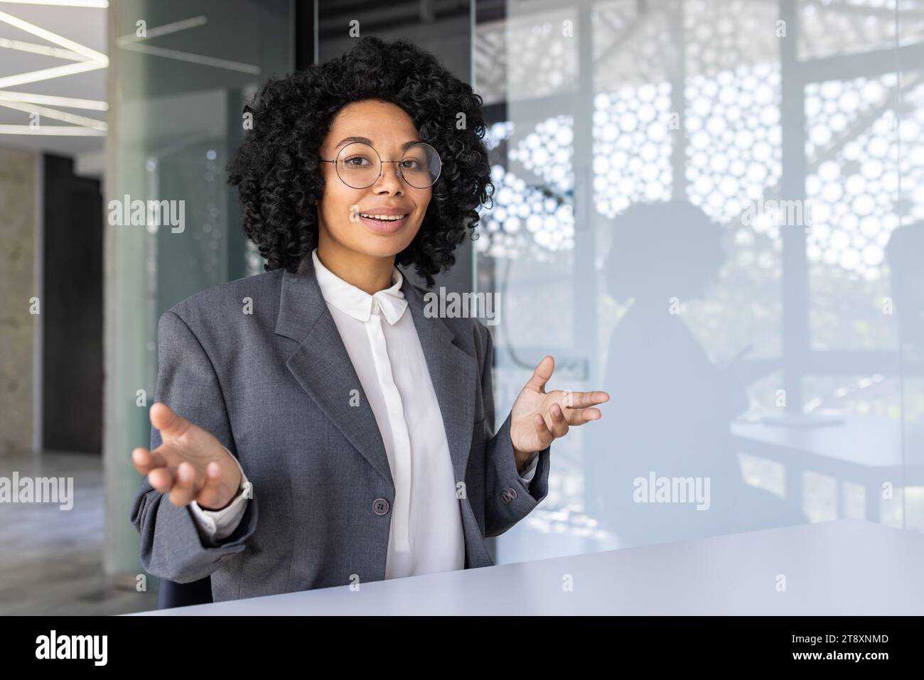 Jeune femme d'affaires afro-américaine faisant la formation, réunion en ligne assise dans le bureau à table, parlant et souriant à la caméra. Banque D'Images