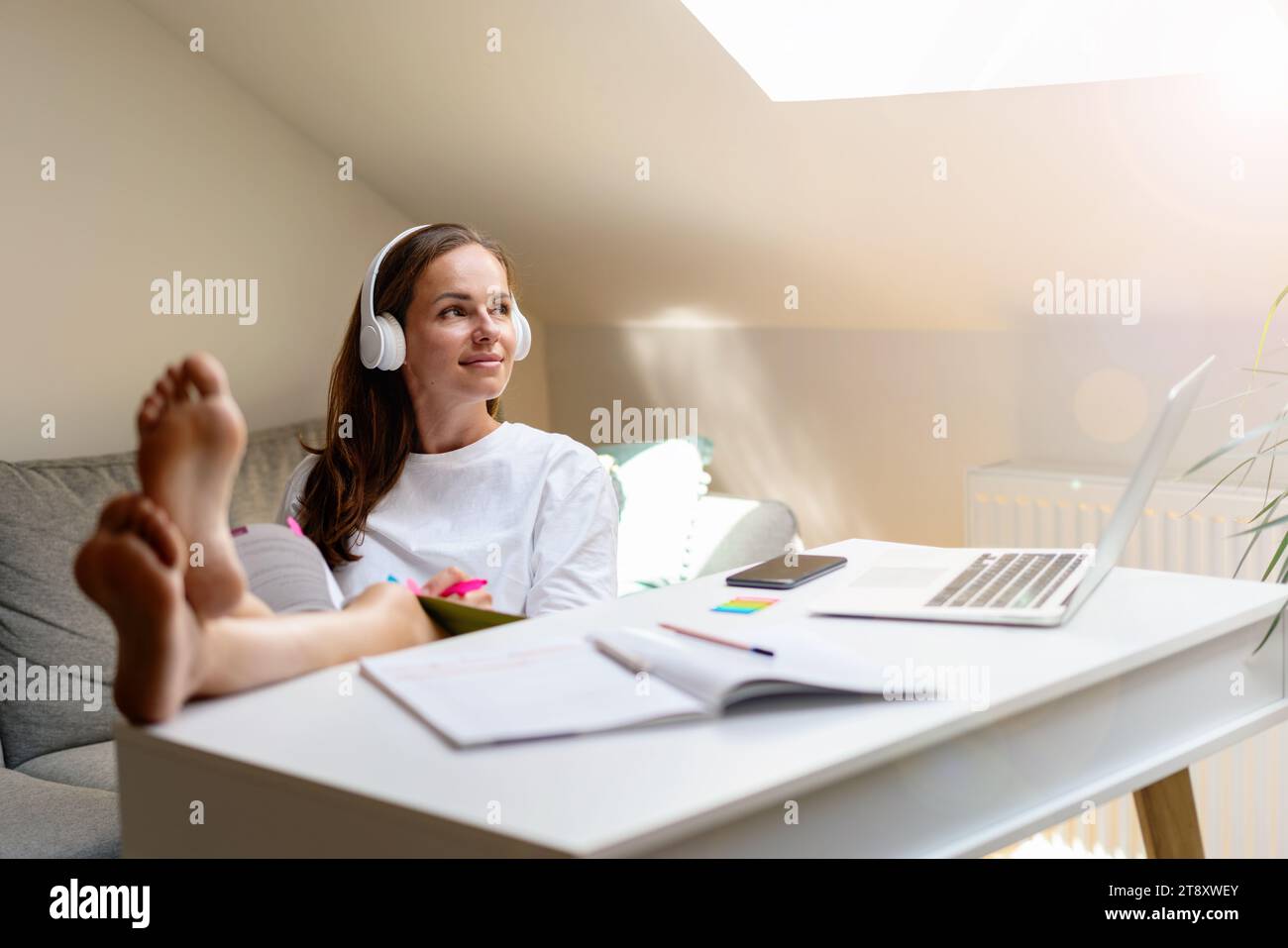 Le mode de vie domestique de l'étudiant. Une jeune femme dans un casque blanc est assise les pieds sur la table. Banque D'Images