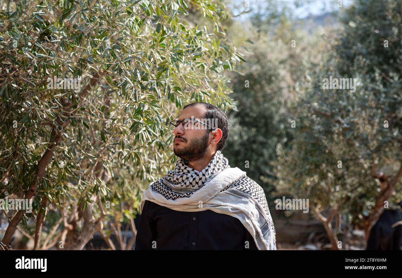 portrait pour homme portant keffiyeh dans le champ d'oliviers avec fond noir et chemises noires également avec expression faciale en colère Banque D'Images