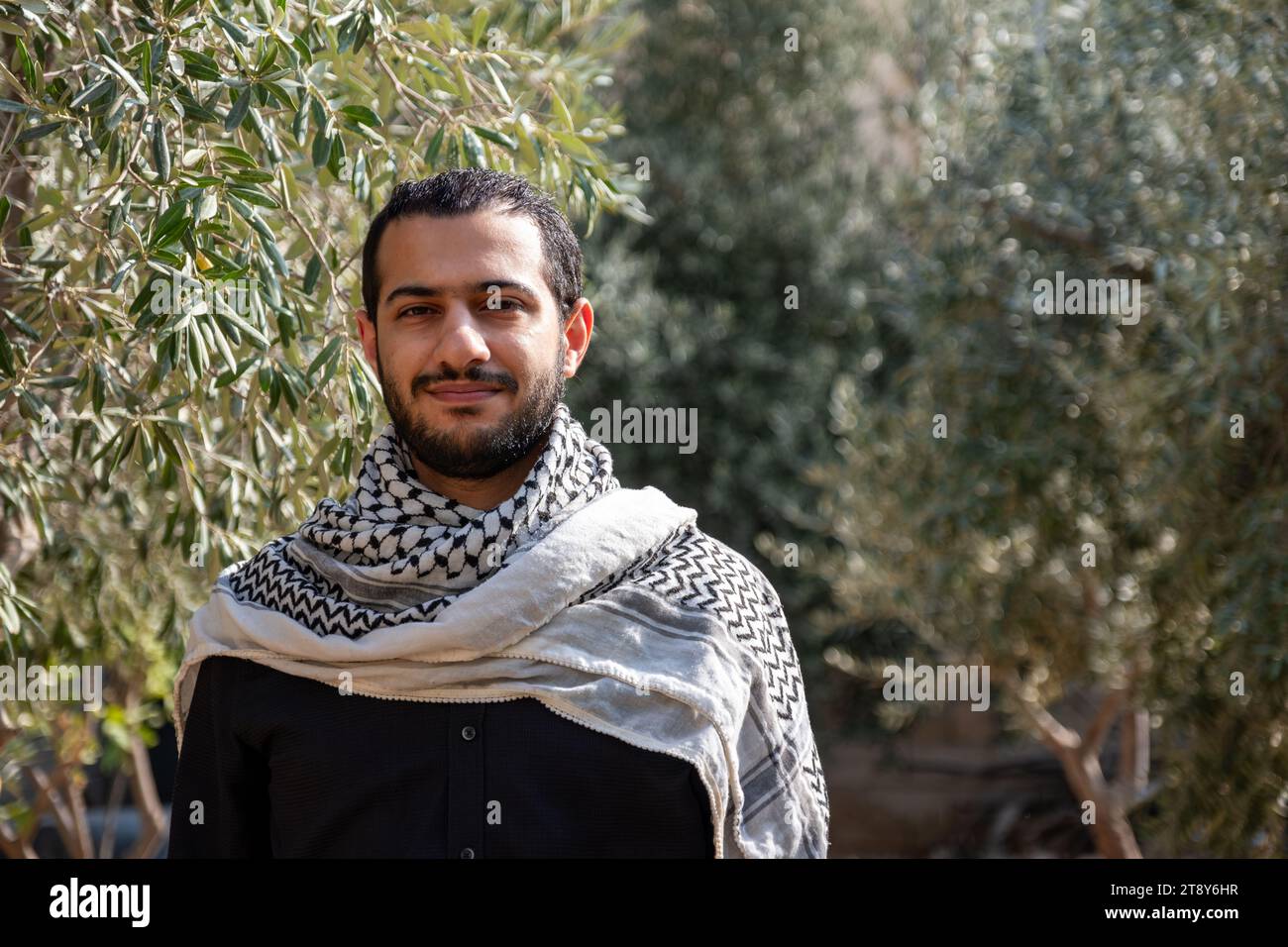 portrait pour homme portant keffiyeh dans le champ d'oliviers avec fond noir et chemises noires également avec expression faciale sourire Banque D'Images