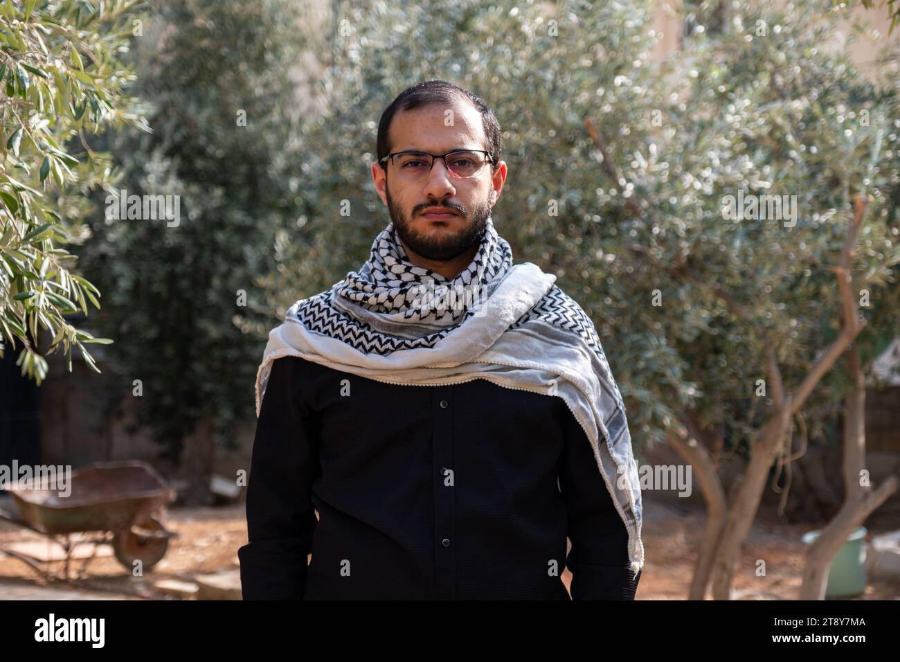 portrait pour homme portant keffiyeh dans le champ d'oliviers avec fond noir et chemises noires également avec expression faciale en colère Banque D'Images