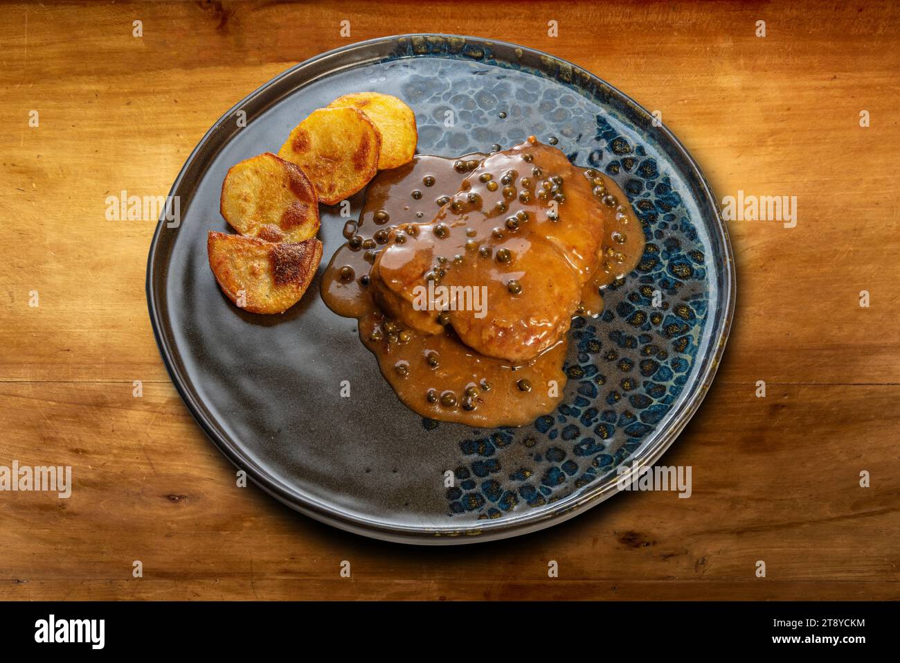 Filet de bœuf au poivre vert avec pommes de terre cuites dans une assiette noire sur une table en bois Banque D'Images