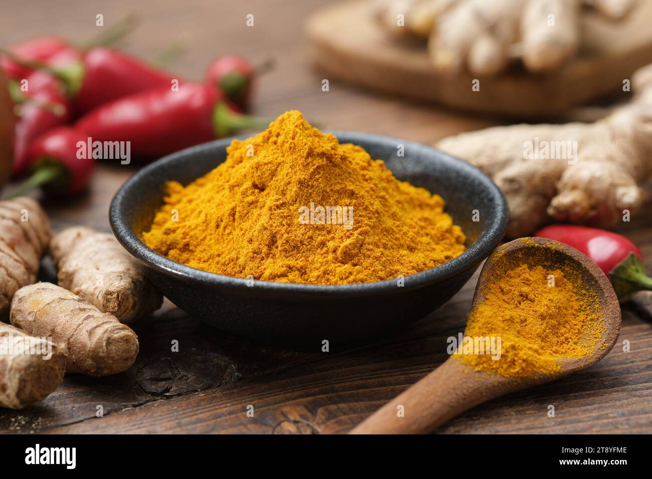 Bol de curcuma moulu en poudre et racines entières de curcuma. Gousses de piment rouge et racines de gingembre sur fond. Ingrédients pour la cuisine et Ayurveda Banque D'Images