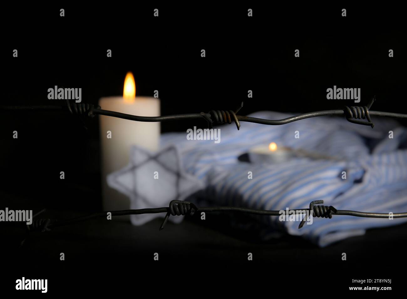 Fil barbelé avec des bougies allumées et uniforme de prisonnier sur fond sombre, gros plan. Journée internationale de commémoration de l'Holocauste Banque D'Images