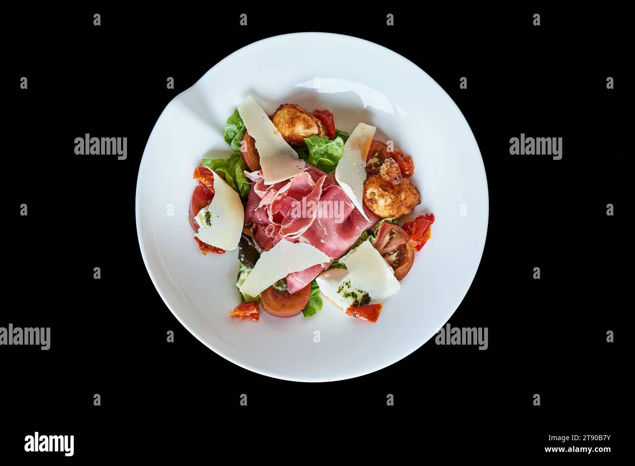 Salade italienne avec jambon cru, tomate et parmesan dans un plat blanc rond sur fond noir, vu de dessus. Banque D'Images
