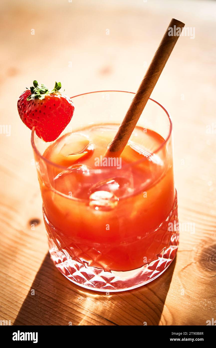 Une vue plongeante d'un cocktail de fruits rouges avec de la glace et de la paille sur une table en bois au soleil d'été. Banque D'Images