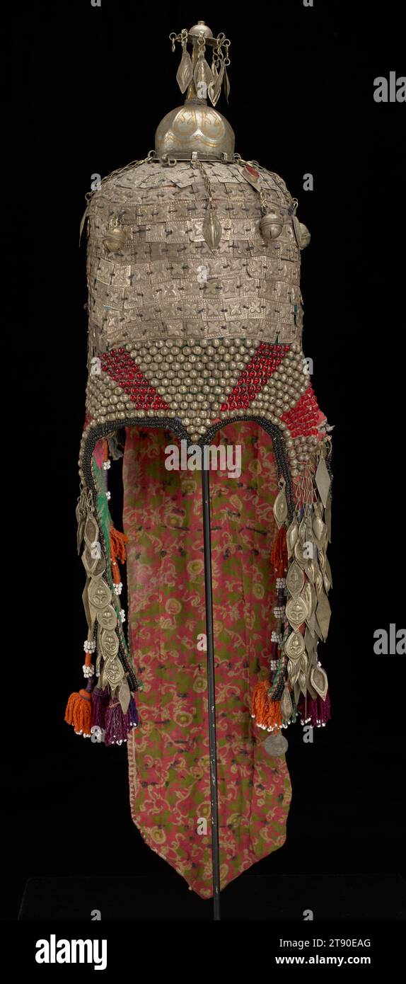 Chapeau, fin 19e-début 20e siècle, 29 7/8 × 9 1/4 × 6 1/2 po. (75,88 × 23,5 × 16,51 cm) (y compris la queue arrière), coton, métal, soie, fils métalliques, perles, cornaline, Ouzbékistan ou Afghanistan, 19e-20e siècle, ce chapeau a été fabriqué par des gens du groupe culturel turkmène d'Asie centrale à la fin du XIXe siècle ou au début du XXe siècle. Il aurait été porté par des femmes d'élite dans le cadre d'un ensemble de mariage traditionnel. Le chapeau combine de nombreux matériaux et techniques distinctifs qui sont représentatifs de la culture. Les pompons coupés, les plaques de métal estampées, et l'utilisation de la cornaline Banque D'Images
