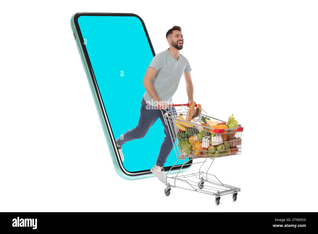 Épicerie via Internet. Homme heureux avec panier plein de produits à court d'énorme smartphone sur fond blanc Banque D'Images