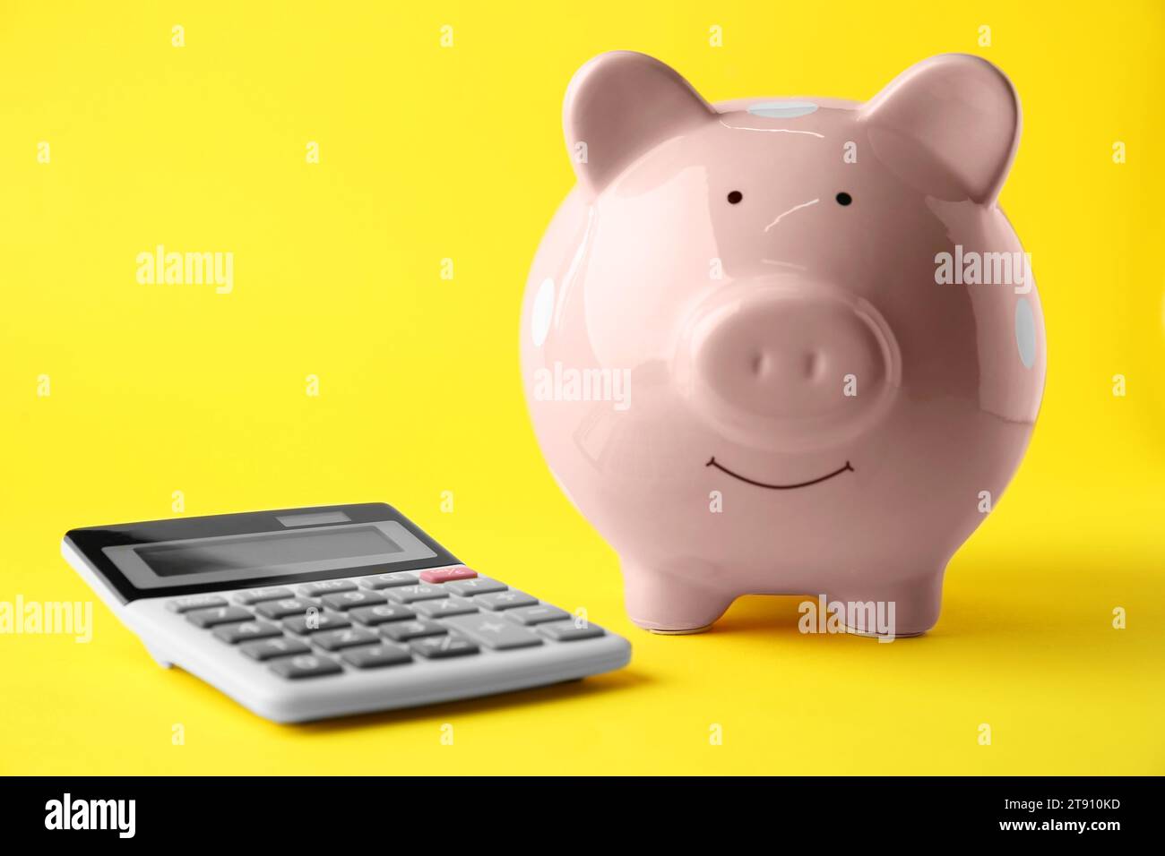 Calculatrice et tirelire rose sur fond jaune, gros plan Banque D'Images