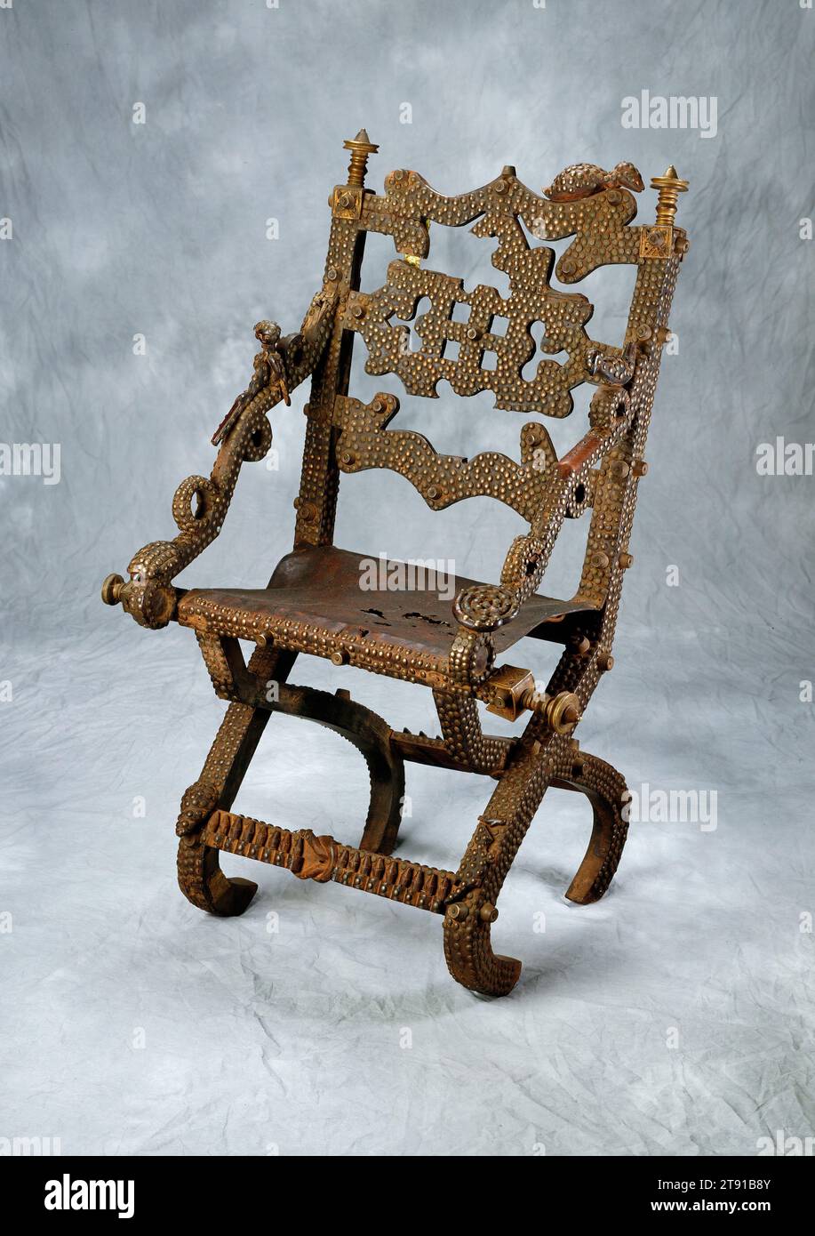 Chaise de chef, 19e siècle, 41 x 29 1/2 x 20 po. (104,1 x 74,9 x 50,8 cm), Bois, cuir, laiton, Ghana, 19e siècle, le peuple Asante du Ghana a développé une « culture des sièges » complexe, avec de nombreux types de tabourets et de chaises employés dans différents contextes. Un siège frappant utilisé par l'aristocratie est la chaise pliante sculptée de manière décorative, probablement basée sur les chaises des premiers voyageurs européens. Son dos est sculpté dans un motif perforé, et toute la surface est recouverte de clous en laiton et de pièces métalliques. Cette chaise est inhabituelle en raison de sa riche imagerie, montrant divers oiseaux, une personne tenant un fusil Banque D'Images