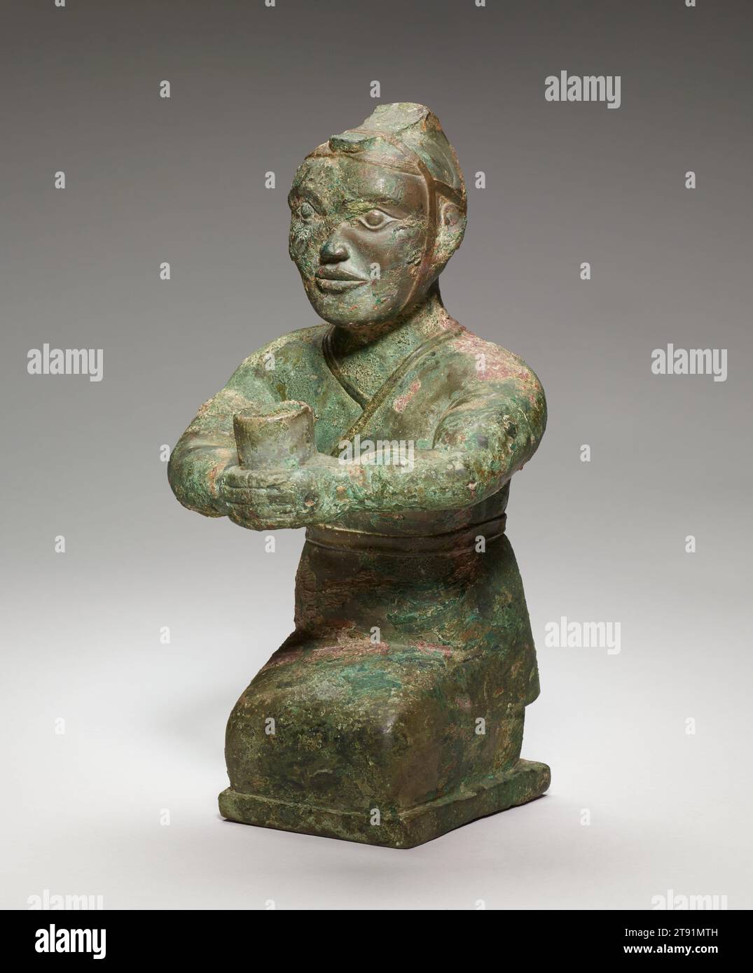 Figurine agenouillée, 4e siècle av. J.-C., 11 1/4 × 6 × 6 po., 7,3 lb. (28,58 × 15,24 × 15,24 cm, 3,3 kg), Bronze, Chine, 4e siècle av. J.-C., fouillée près de Luoyang, la capitale de la dynastie Zhou orientale (770–256 av. J.-C.), cette petite sculpture d'un homme agenouillé tenant un vaisseau en forme de tube dans ses mains étendues peut avoir servi de porte-torche dans une tombe. La figurine est vêtue d'un vêtement ajusté qui s'enroule de gauche à droite et est ceinturé avec une bande étroite. Le couvre-tête, un peu comme un casque ouvert, est large à l'arrière et monte à un sommet pointu avant de descendre dans une bande étroite en forme de langue Banque D'Images