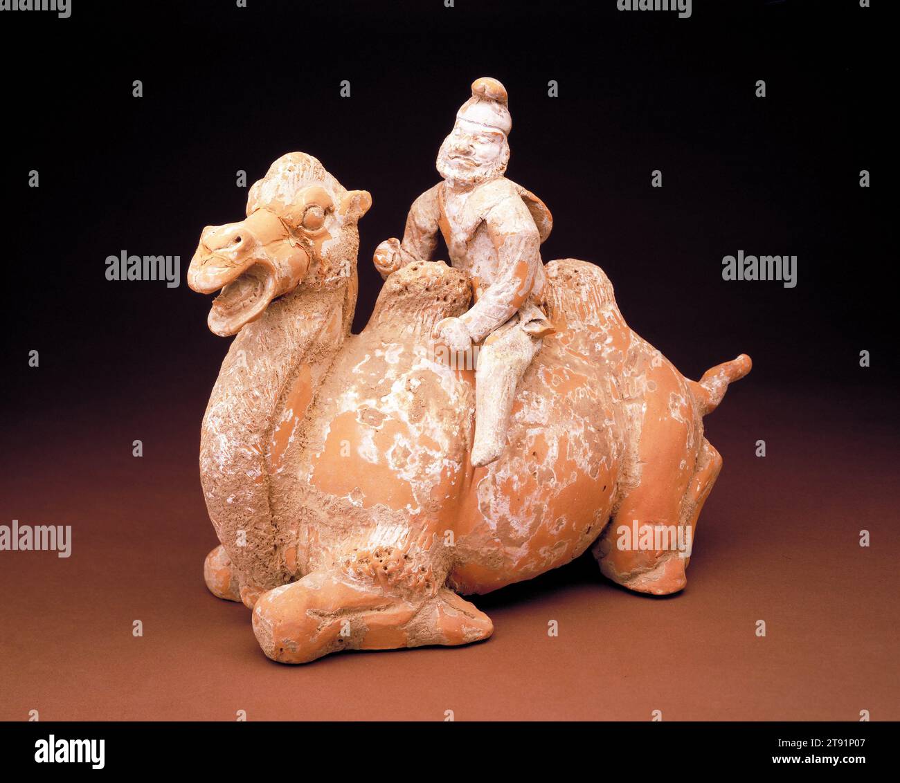 Tombe Figure d'un chameau agenouillé avec pilote, 618-906, 9 3/4 x 13 po. (24,77 x 33,02 cm), faïence rouge avec des traces de glissement et de polychromie, Chine, 7e-10e siècle, ce chameau de Bactriane bien modelé et son pilote d'Asie centrale reflètent la nature cosmopolite de l'art Tang Le chameau était la principale bête du fardeau le long des grandes routes caravanières qui reliaient la Chine Tang à l'Asie centrale et au Moyen-Orient. Cette bête sournoise, ainsi que les différents peuples étrangers qui envahissaient les grands marchés de CH'ang-an et Lo-yang, sont devenus des sujets favoris et exotiques pour les potiers Tang observants Banque D'Images