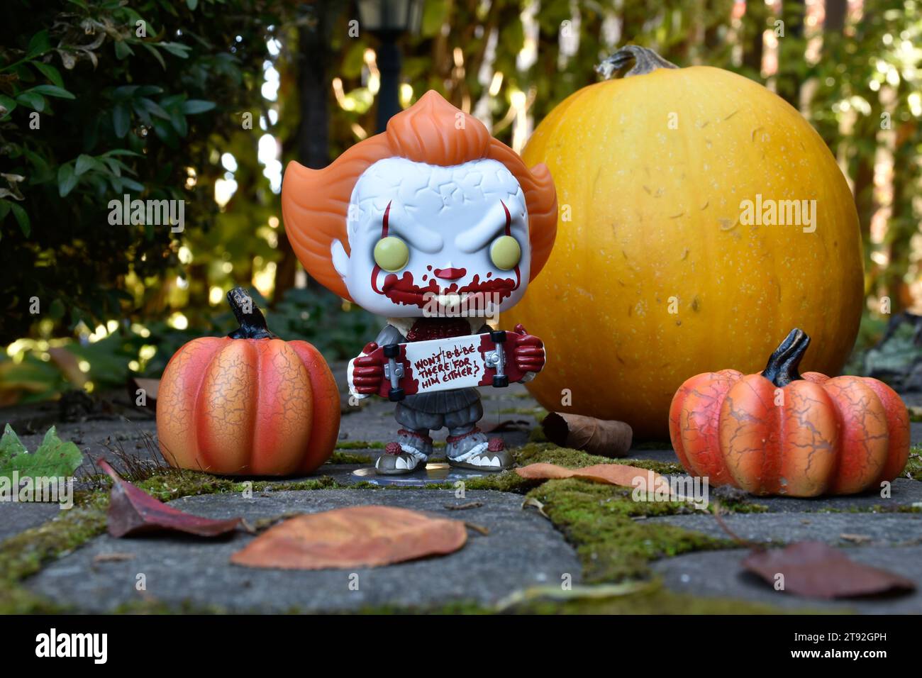 Funko Pop figurine d'action de Pennywise mal clown avec planche à roulettes sanglante du film d'horreur IT. Halloween, saison effrayante, citrouilles, mousse, feuilles d'automne. Banque D'Images