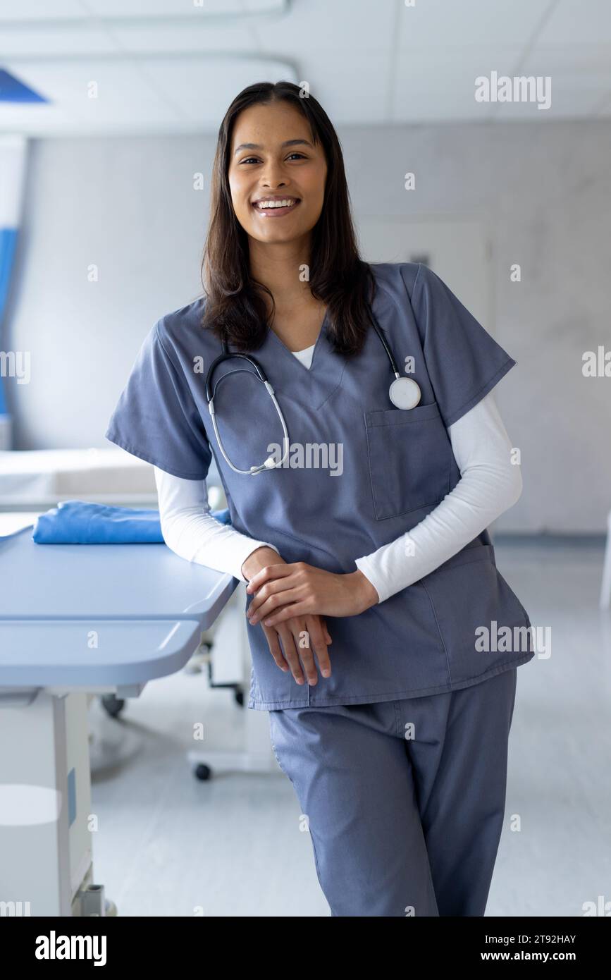 Portrait d'une femme biraciale heureuse médecin dans une chambre d'hôpital ensoleillée Banque D'Images